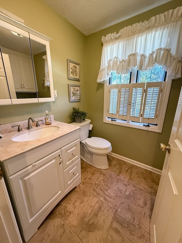 half bath featuring vanity, toilet, baseboards, and a textured ceiling