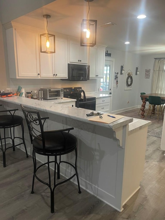 kitchen featuring wood finished floors, a peninsula, white cabinets, a kitchen breakfast bar, and black electric range oven