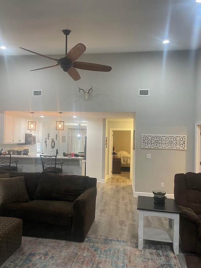 living area featuring ceiling fan, visible vents, a towering ceiling, and light wood finished floors