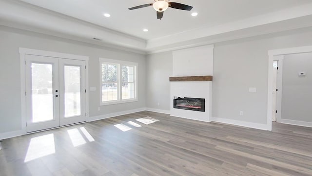 unfurnished living room with light hardwood / wood-style flooring, ceiling fan, ornamental molding, french doors, and a raised ceiling