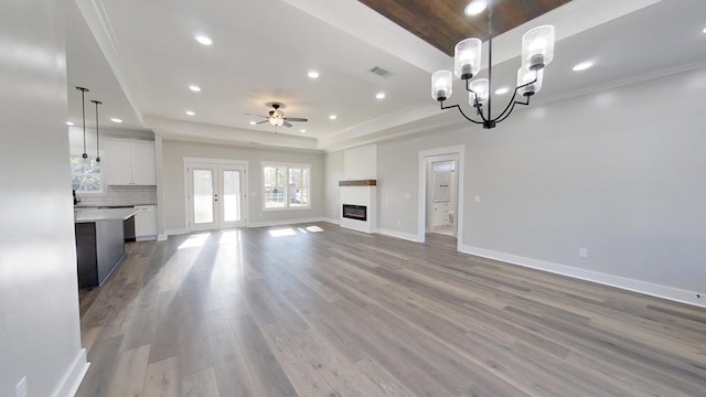 unfurnished living room with hardwood / wood-style floors, ceiling fan with notable chandelier, and a raised ceiling