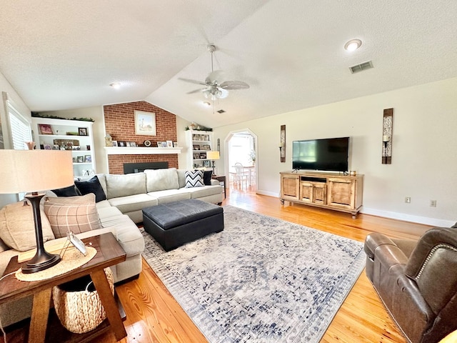 living room with lofted ceiling, ceiling fan, light wood-type flooring, a textured ceiling, and a fireplace