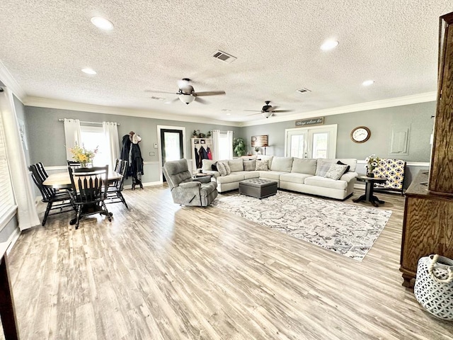 living room with a textured ceiling, light hardwood / wood-style flooring, ceiling fan, and crown molding