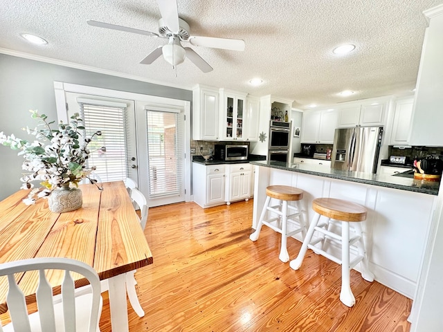 kitchen featuring white cabinets, light wood-type flooring, ornamental molding, appliances with stainless steel finishes, and kitchen peninsula