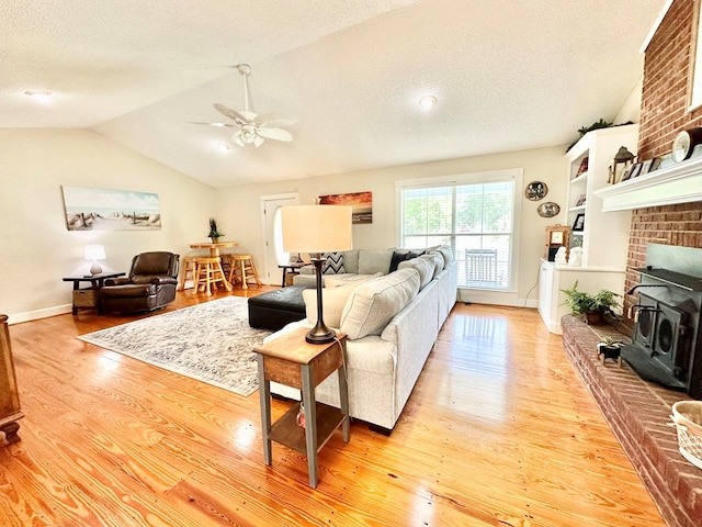 living room with a textured ceiling, a wood stove, light hardwood / wood-style flooring, and vaulted ceiling