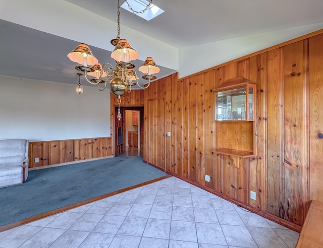 spare room with a chandelier, lofted ceiling with skylight, wooden walls, and light colored carpet