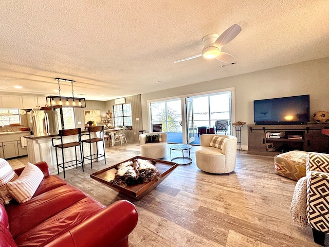 living room with ceiling fan, a textured ceiling, and light wood-type flooring