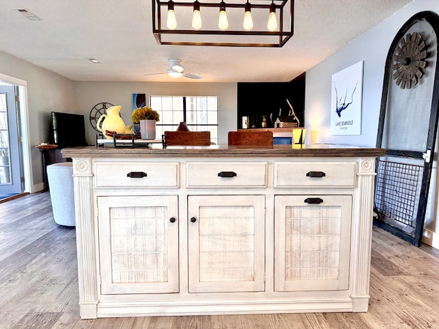 kitchen with a kitchen island, light wood-type flooring, white cabinets, ceiling fan, and a textured ceiling