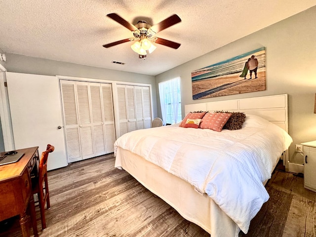 bedroom featuring two closets, wood-type flooring, a textured ceiling, and ceiling fan