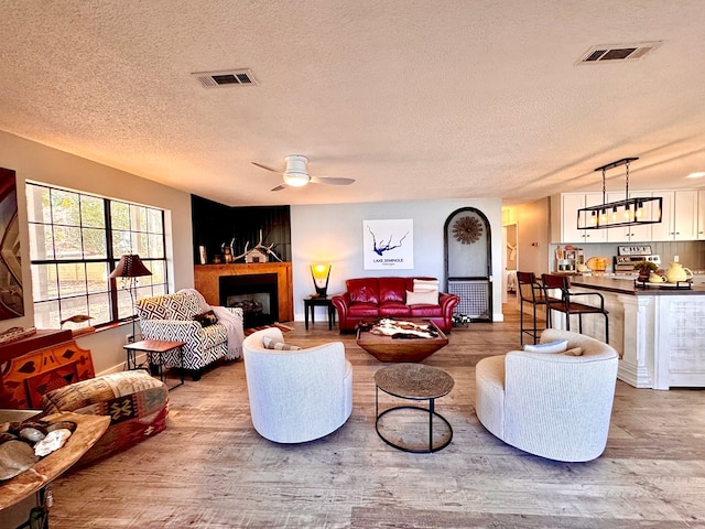 living room with a textured ceiling, light hardwood / wood-style floors, and ceiling fan