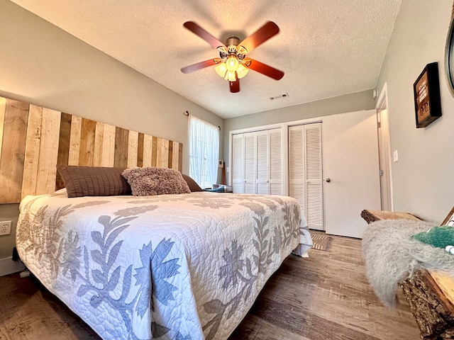 bedroom with ceiling fan, dark hardwood / wood-style floors, a textured ceiling, and two closets