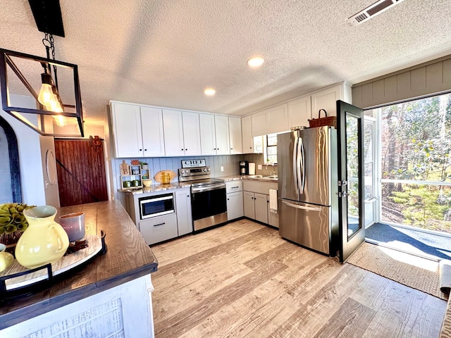 kitchen featuring white cabinetry, decorative light fixtures, light wood-type flooring, and appliances with stainless steel finishes