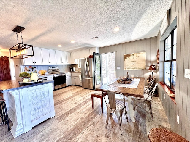 kitchen featuring a textured ceiling, light wood-type flooring, appliances with stainless steel finishes, pendant lighting, and white cabinets