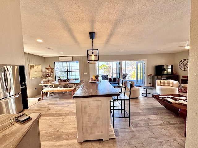 kitchen featuring a breakfast bar, a textured ceiling, light wood-type flooring, stainless steel refrigerator, and pendant lighting