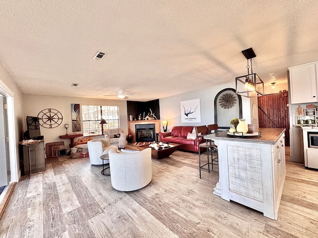 living room with ceiling fan, a textured ceiling, and light hardwood / wood-style floors