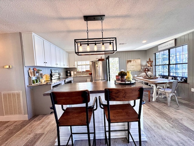 kitchen with appliances with stainless steel finishes, decorative light fixtures, white cabinets, a textured ceiling, and light hardwood / wood-style flooring