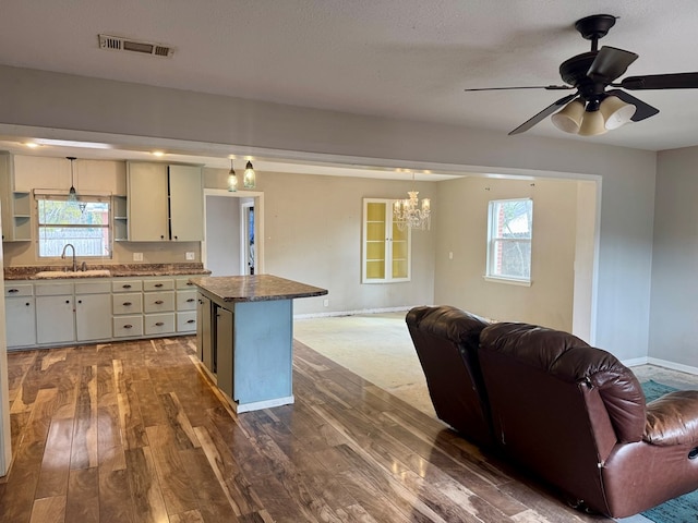 kitchen featuring sink, dark stone countertops, a kitchen island, dark hardwood / wood-style flooring, and decorative light fixtures