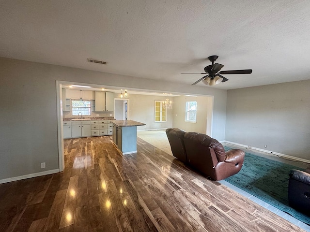 unfurnished living room featuring wood-type flooring, sink, ceiling fan, and a textured ceiling