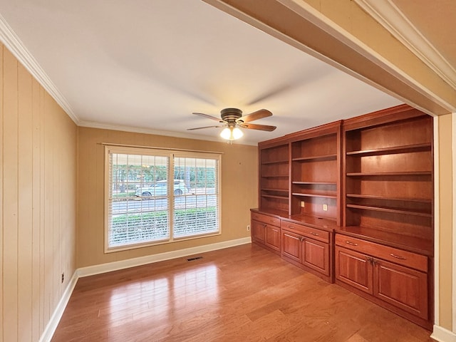 unfurnished living room with ornamental molding, ceiling fan, light hardwood / wood-style floors, and wooden walls