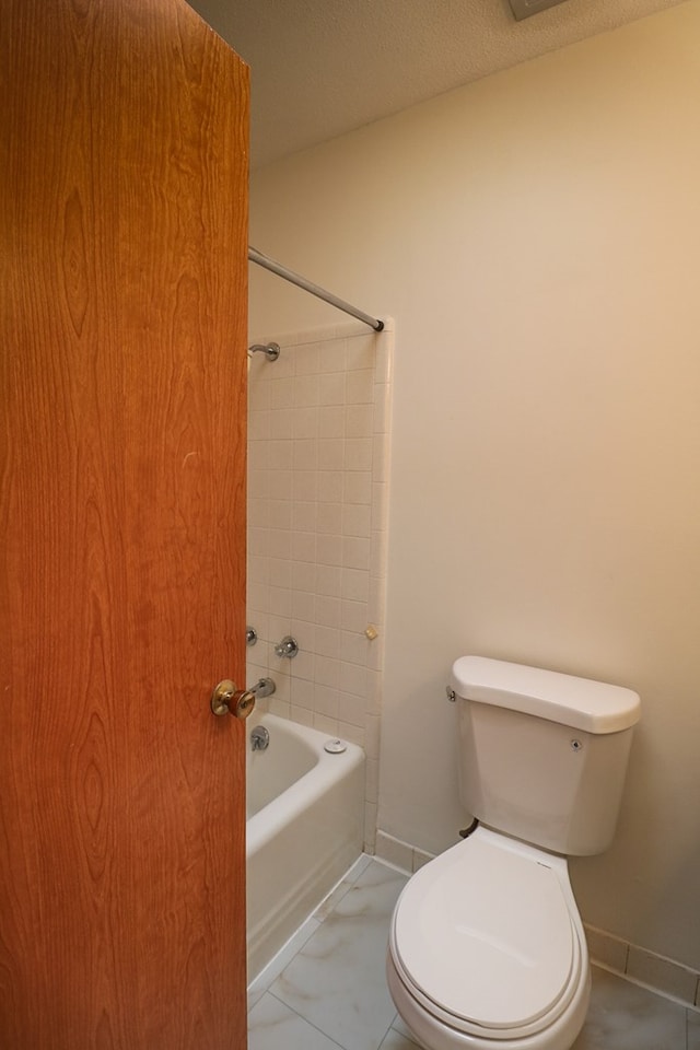 bathroom featuring tile patterned flooring, tiled shower / bath, a textured ceiling, and toilet