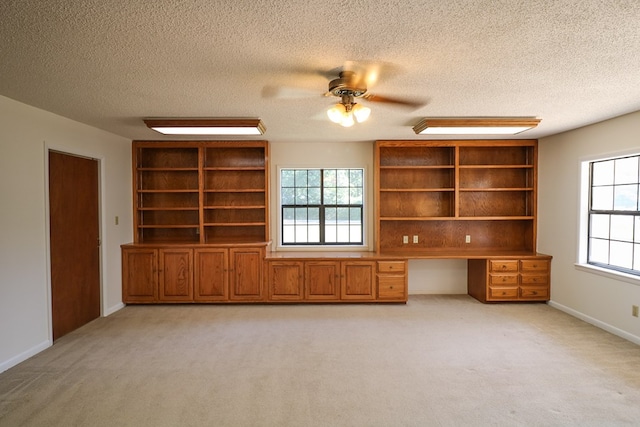 unfurnished living room featuring a textured ceiling, built in desk, and light colored carpet