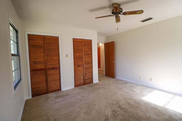 unfurnished bedroom with ceiling fan, light colored carpet, and two closets