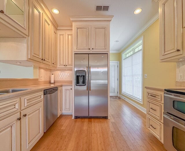 115 Lakeside Ln, Bainbridge, GA 39819 - kitchen featuring appliances with stainless steel finishes, ornamental molding, tasteful backsplash, light countertops, and light wood-style floors
