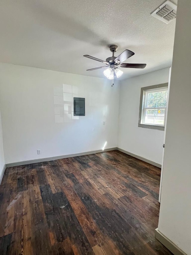 empty room with a textured ceiling, ceiling fan, dark wood-type flooring, and electric panel