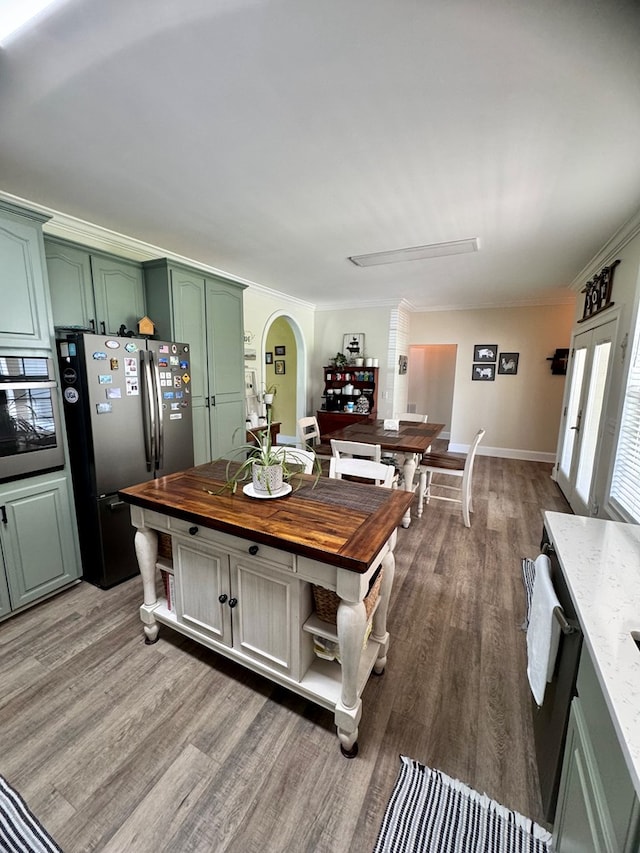 kitchen with appliances with stainless steel finishes, hardwood / wood-style flooring, green cabinetry, and ornamental molding