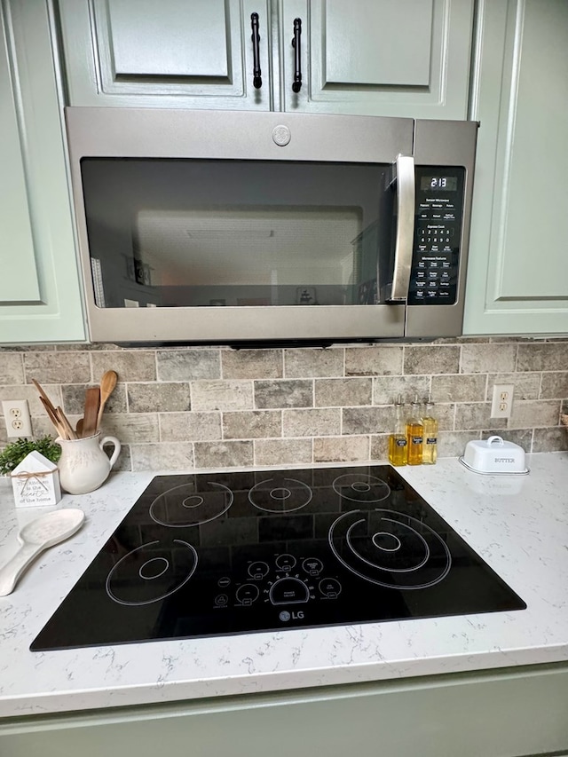 details featuring green cabinets, decorative backsplash, black electric stovetop, and light stone countertops