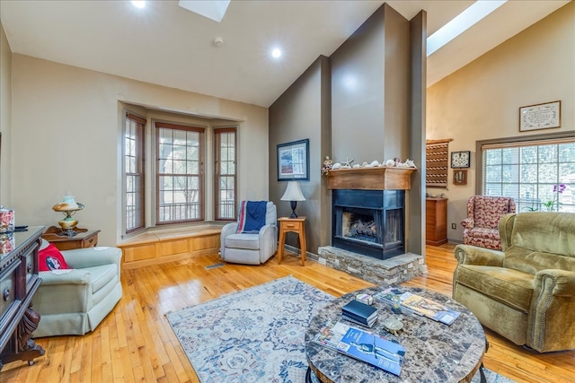 living room with a fireplace with raised hearth, high vaulted ceiling, and hardwood / wood-style floors