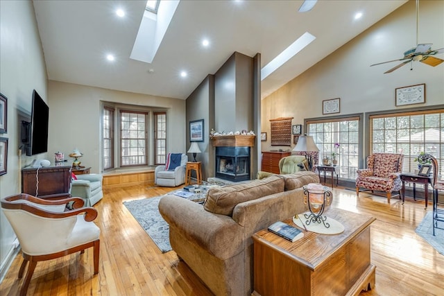 living area featuring a skylight, a large fireplace, ceiling fan, high vaulted ceiling, and light wood-type flooring