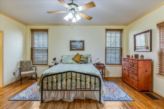 bedroom featuring baseboards, wood finished floors, visible vents, and crown molding