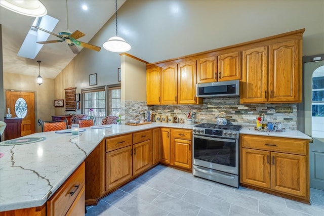 kitchen with a peninsula, a skylight, appliances with stainless steel finishes, brown cabinets, and light stone countertops