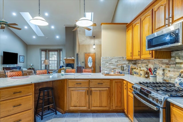 kitchen featuring a skylight, a ceiling fan, appliances with stainless steel finishes, open floor plan, and light stone countertops