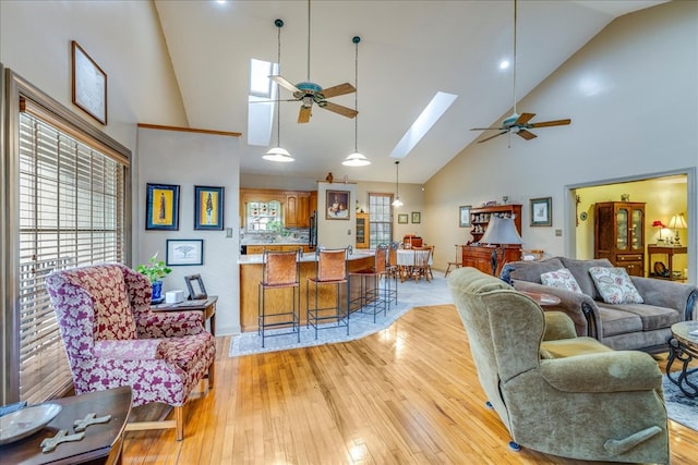 living room with a ceiling fan, a skylight, light wood-type flooring, and plenty of natural light