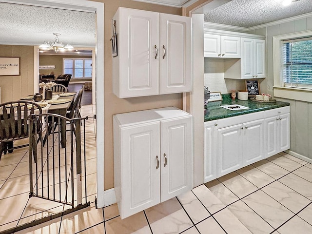 kitchen featuring dark countertops, crown molding, an inviting chandelier, a textured ceiling, and white cabinetry