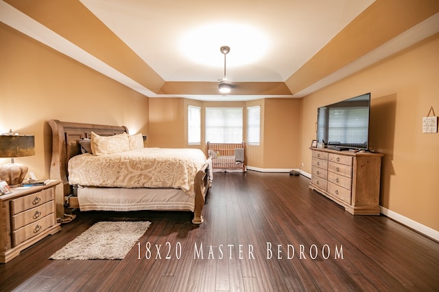 bedroom with dark hardwood / wood-style floors, ceiling fan, and a tray ceiling