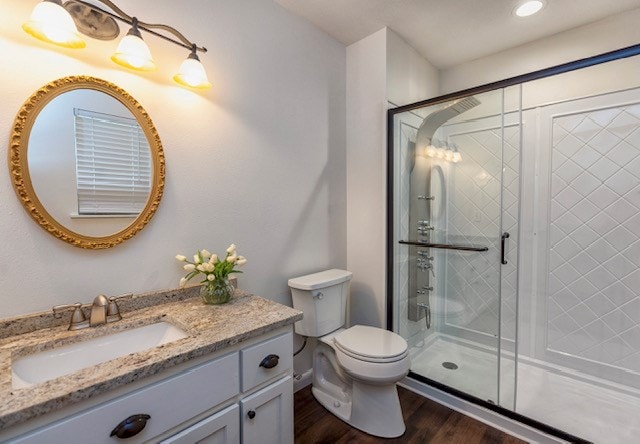 bathroom featuring vanity, wood-type flooring, a shower with shower door, and toilet