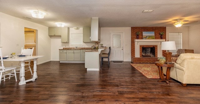 kitchen with dark wood-type flooring, sink, ceiling fan, a fireplace, and kitchen peninsula