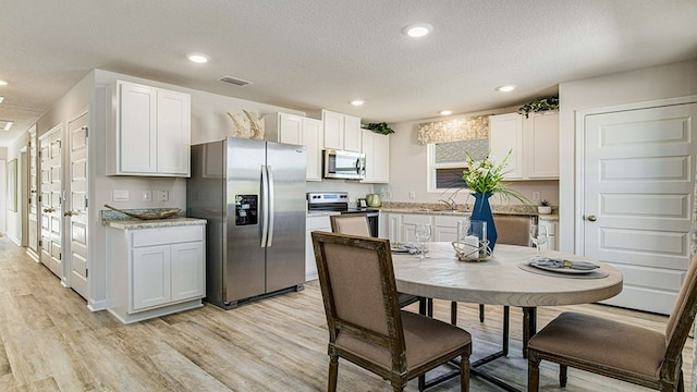 kitchen featuring light hardwood / wood-style flooring, a textured ceiling, appliances with stainless steel finishes, plenty of natural light, and white cabinetry