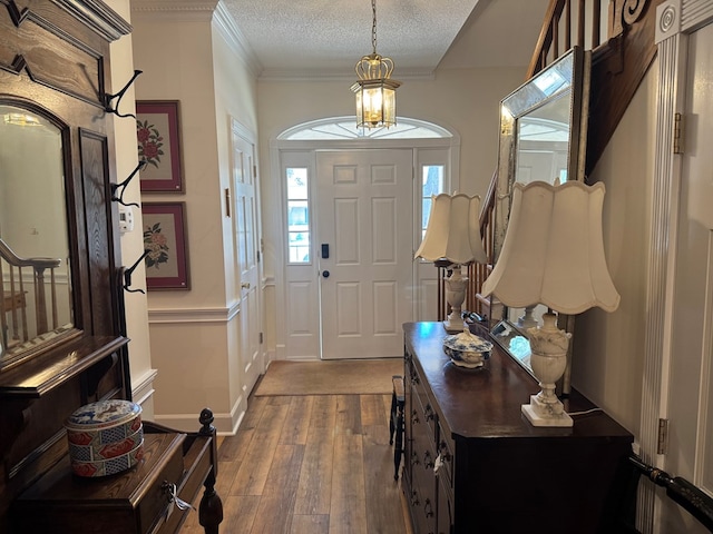 entrance foyer featuring baseboards, a textured ceiling, ornamental molding, and wood finished floors