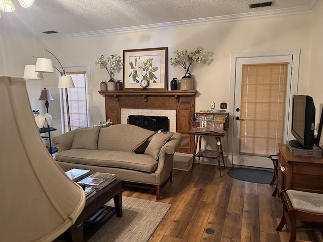 living area featuring a textured ceiling, a fireplace, visible vents, ornamental molding, and dark wood-style floors