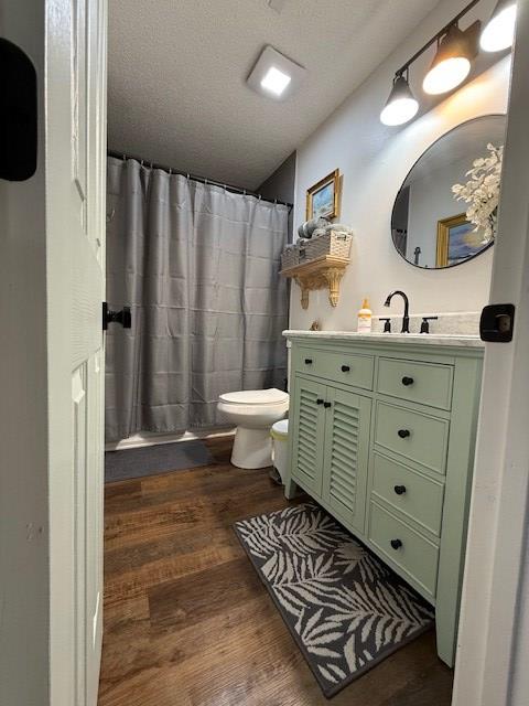 bathroom with wood-type flooring, a textured ceiling, toilet, vanity, and a shower with shower curtain