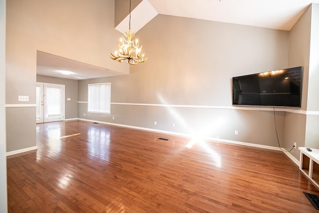 unfurnished living room featuring high vaulted ceiling, a chandelier, and hardwood / wood-style flooring