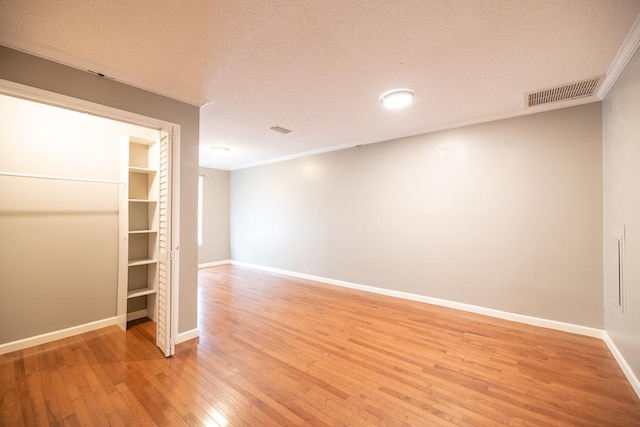 spare room with a textured ceiling, light wood-type flooring, and crown molding