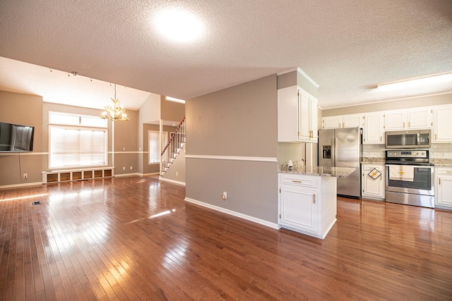 kitchen with white cabinets, dark hardwood / wood-style floors, a textured ceiling, appliances with stainless steel finishes, and light stone counters