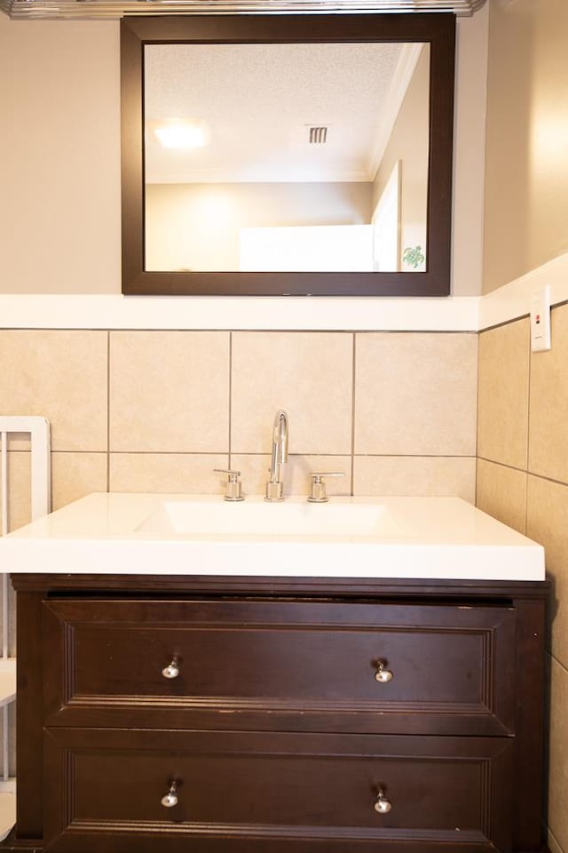 bathroom featuring vanity, crown molding, decorative backsplash, a textured ceiling, and tile walls