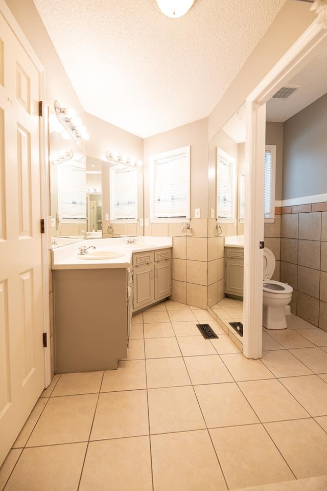 bathroom featuring toilet, a textured ceiling, tile patterned floors, and tile walls