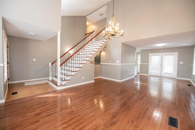 unfurnished living room featuring a chandelier, hardwood / wood-style floors, a towering ceiling, and french doors